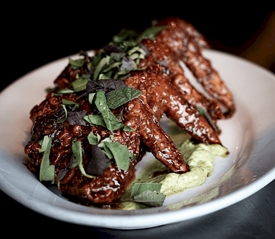 Chicken wings from Detroit's cult-favorite restaurant, Flowers of Vietnam, sit atop creamy cilantro sauce on a white plate